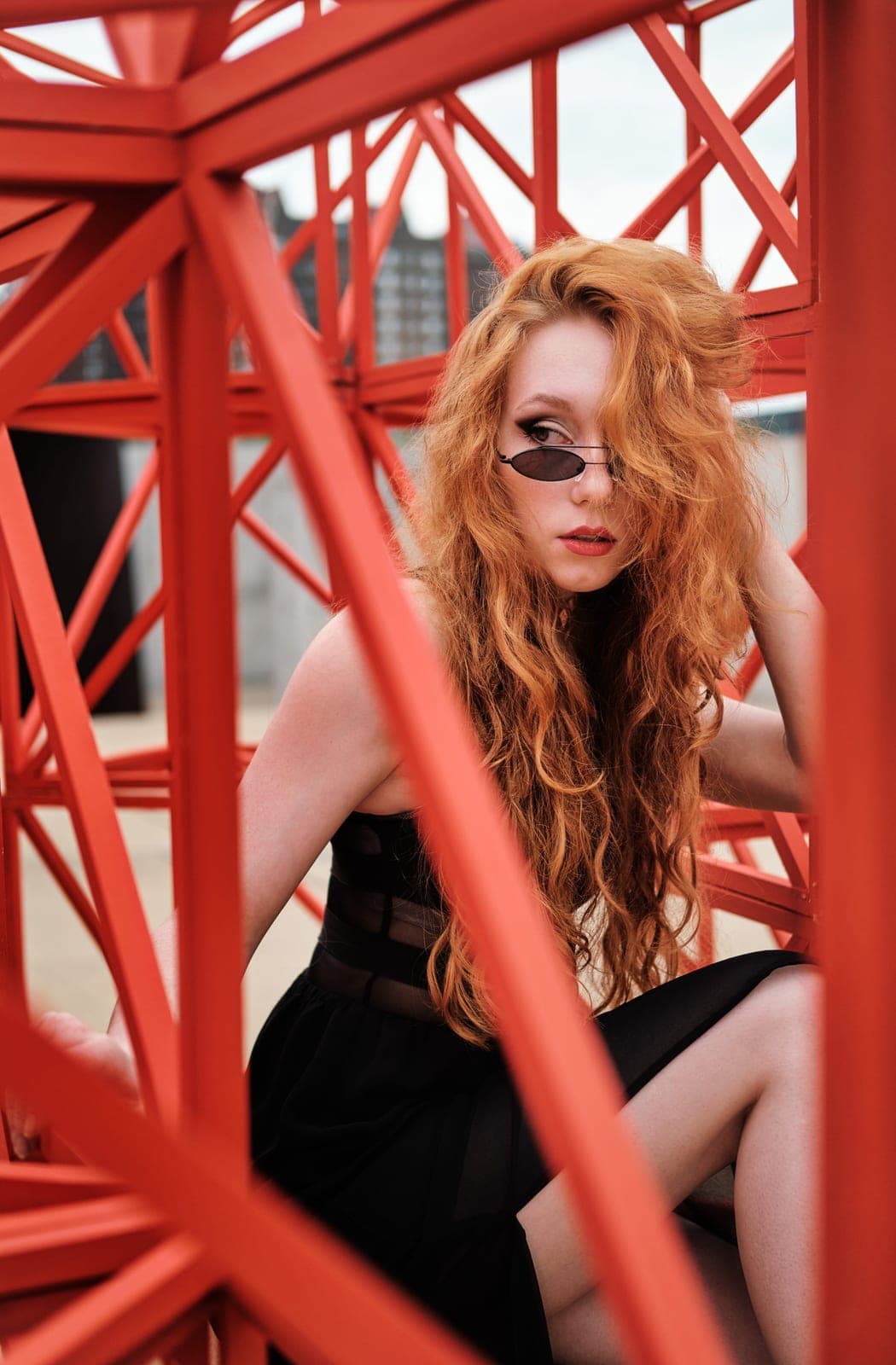 Editorial portrait commission by Henry David: red hair and sunglasses framed by red painted steel beams