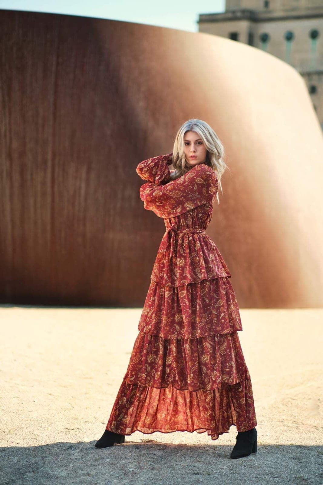 Editorial portrait commission by Henry David: rust patterned gown against a curved steel wall in warm afternoon light