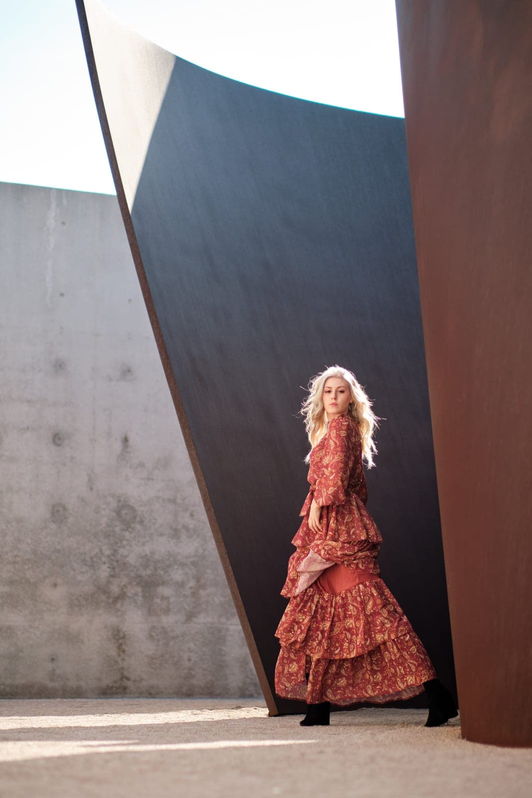 Full-length editorial portrait commission by Henry David: rust patterned gown against a towering sculptural steel wall