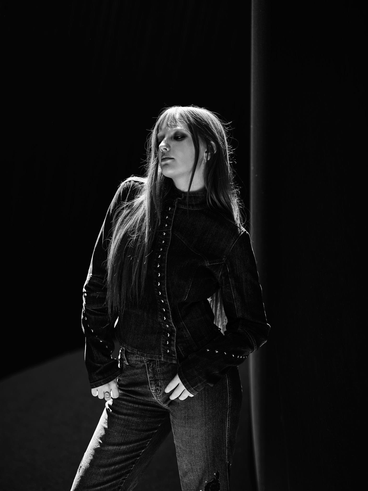 Fine art black and white portrait, dramatic backlit rim light against a dark wall, cinematic chiaroscuro by Henry David