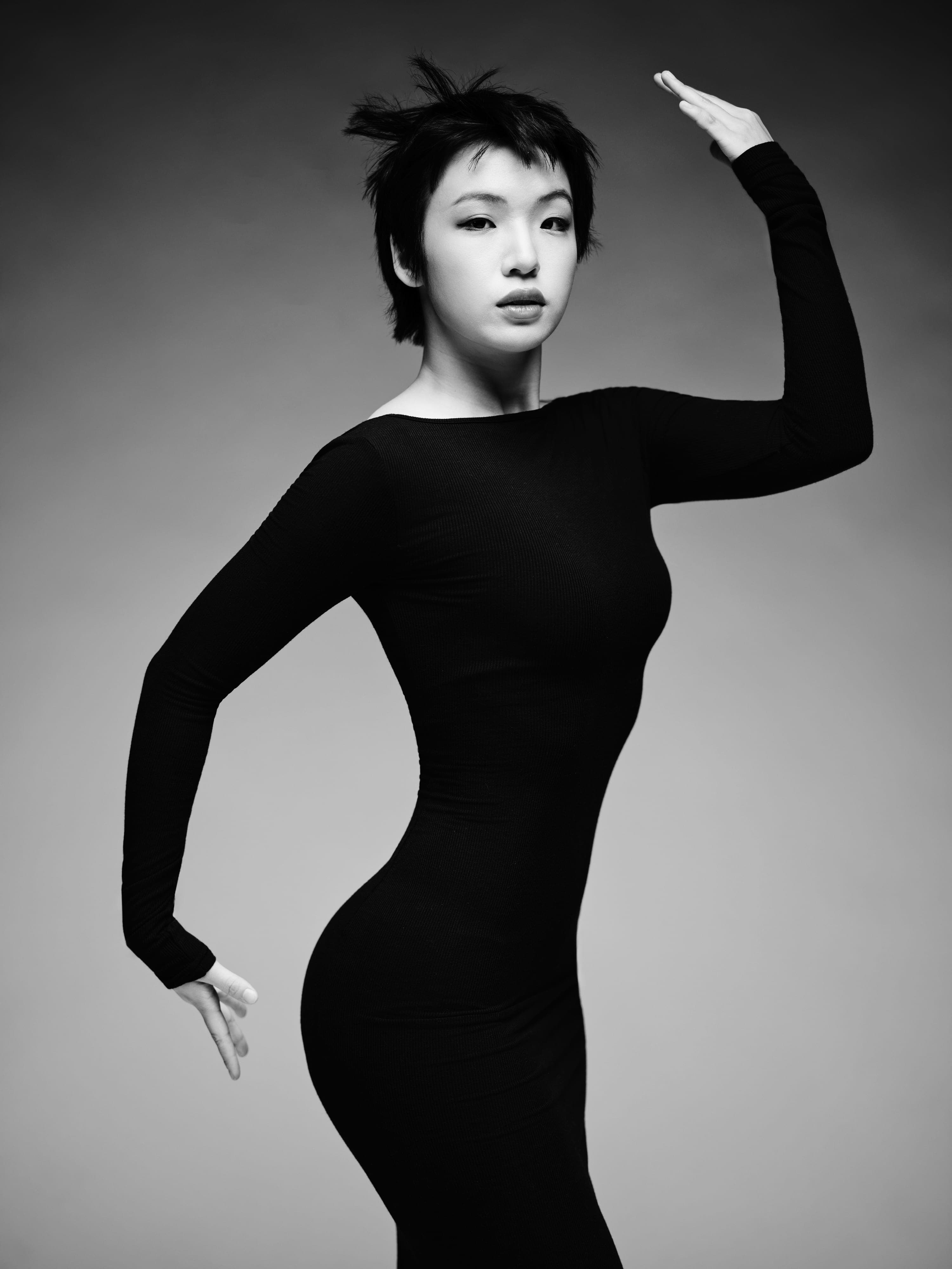 Alice Xu in a long-sleeved black dress with one arm raised, hand on her hip, black and white