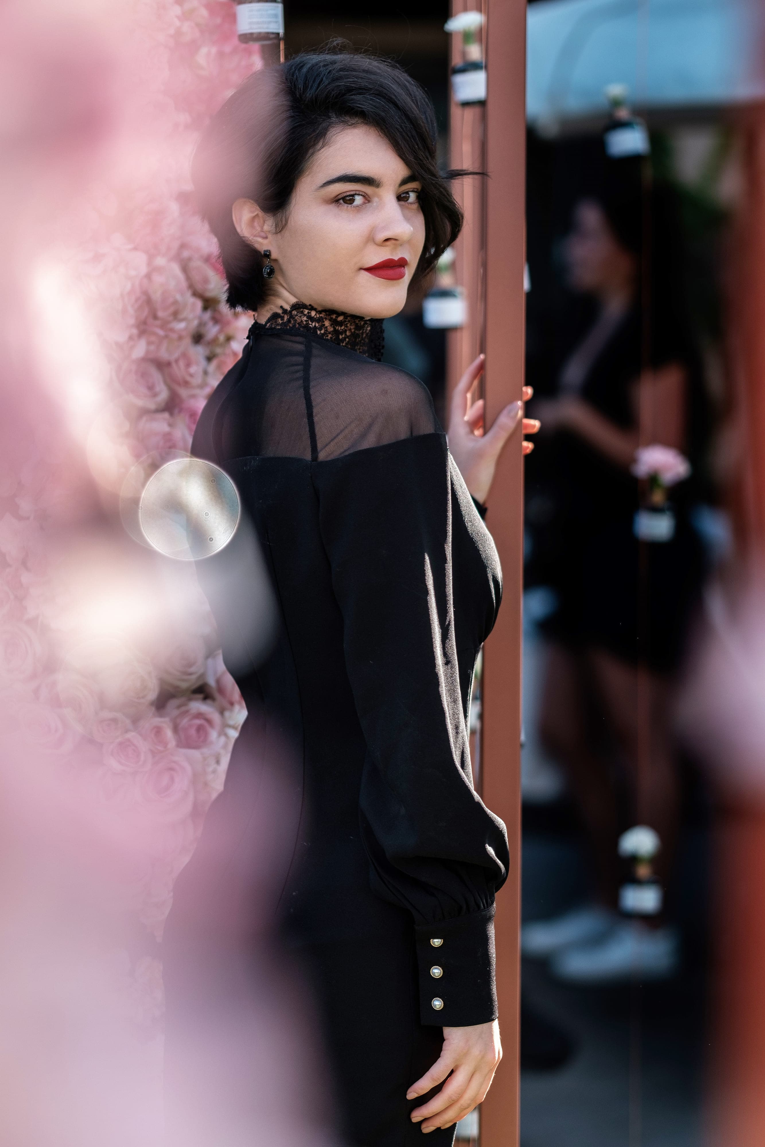 Elly Fileva in a black lace ByBlythe dress among pink blossoms, red lips, short dark hair