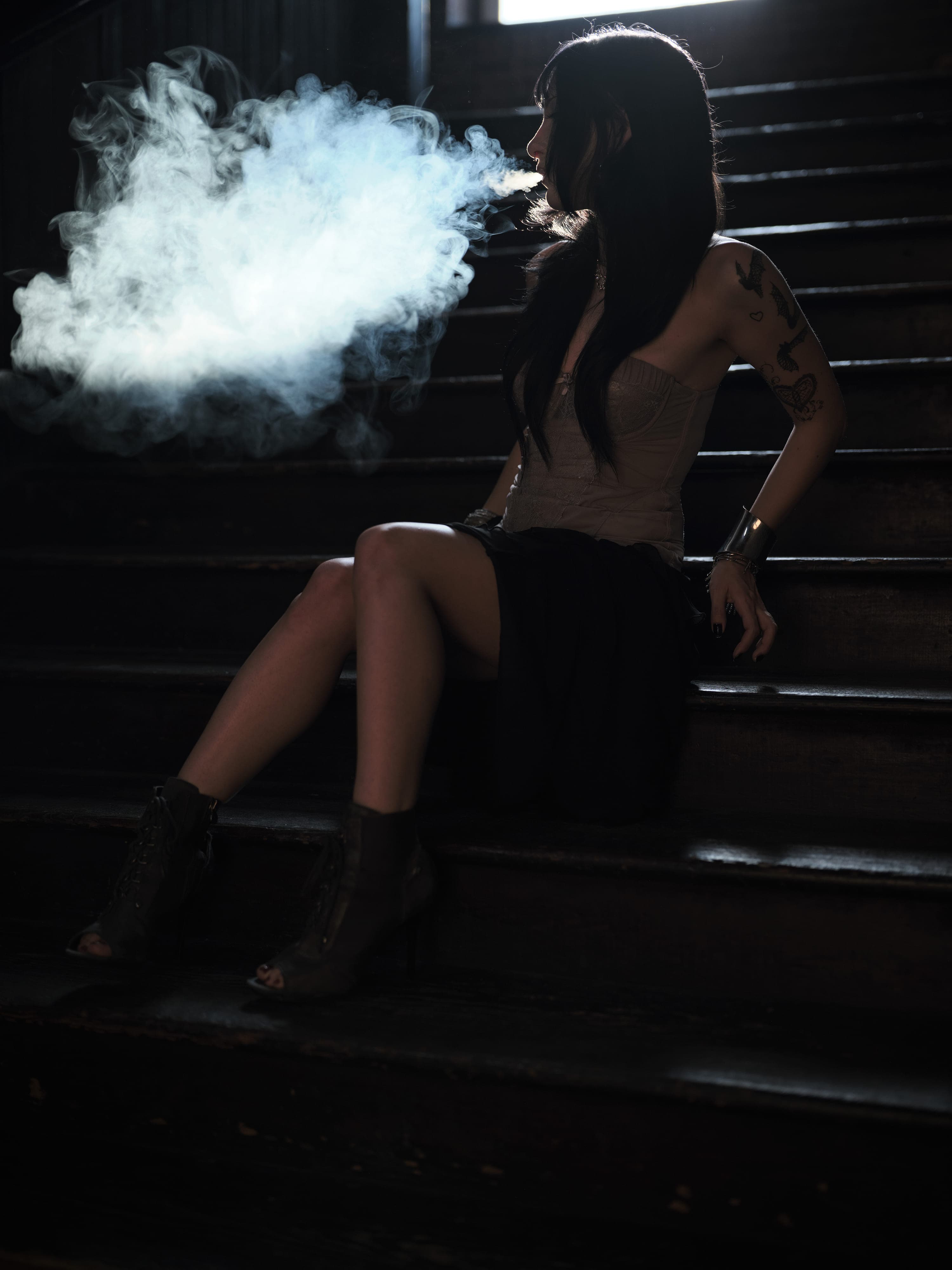 Charlize exhaling smoke on a dark staircase, black and white