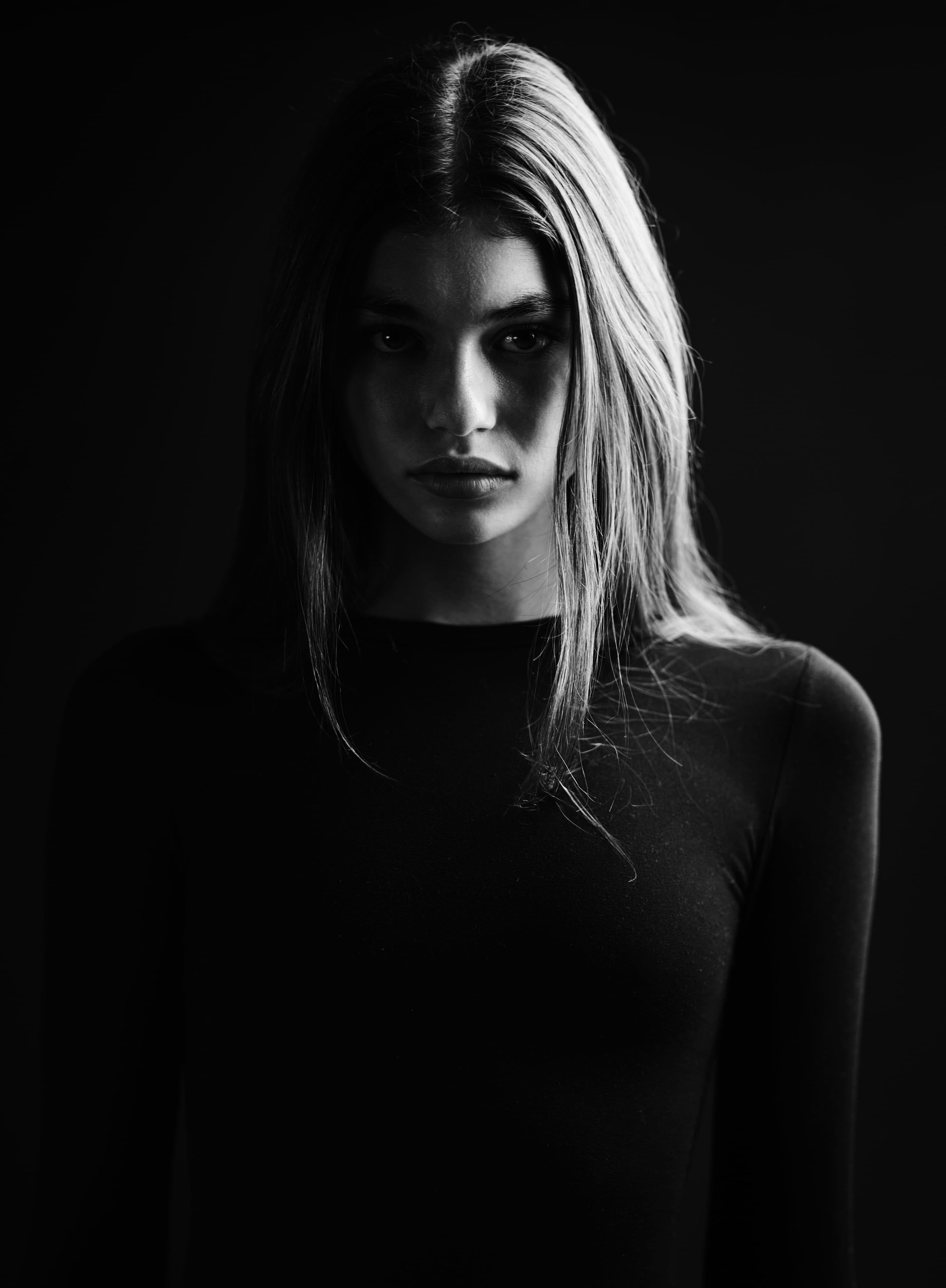 Emme Starkey close in low light, hair falling over one side of her face, black long-sleeved top, black and white