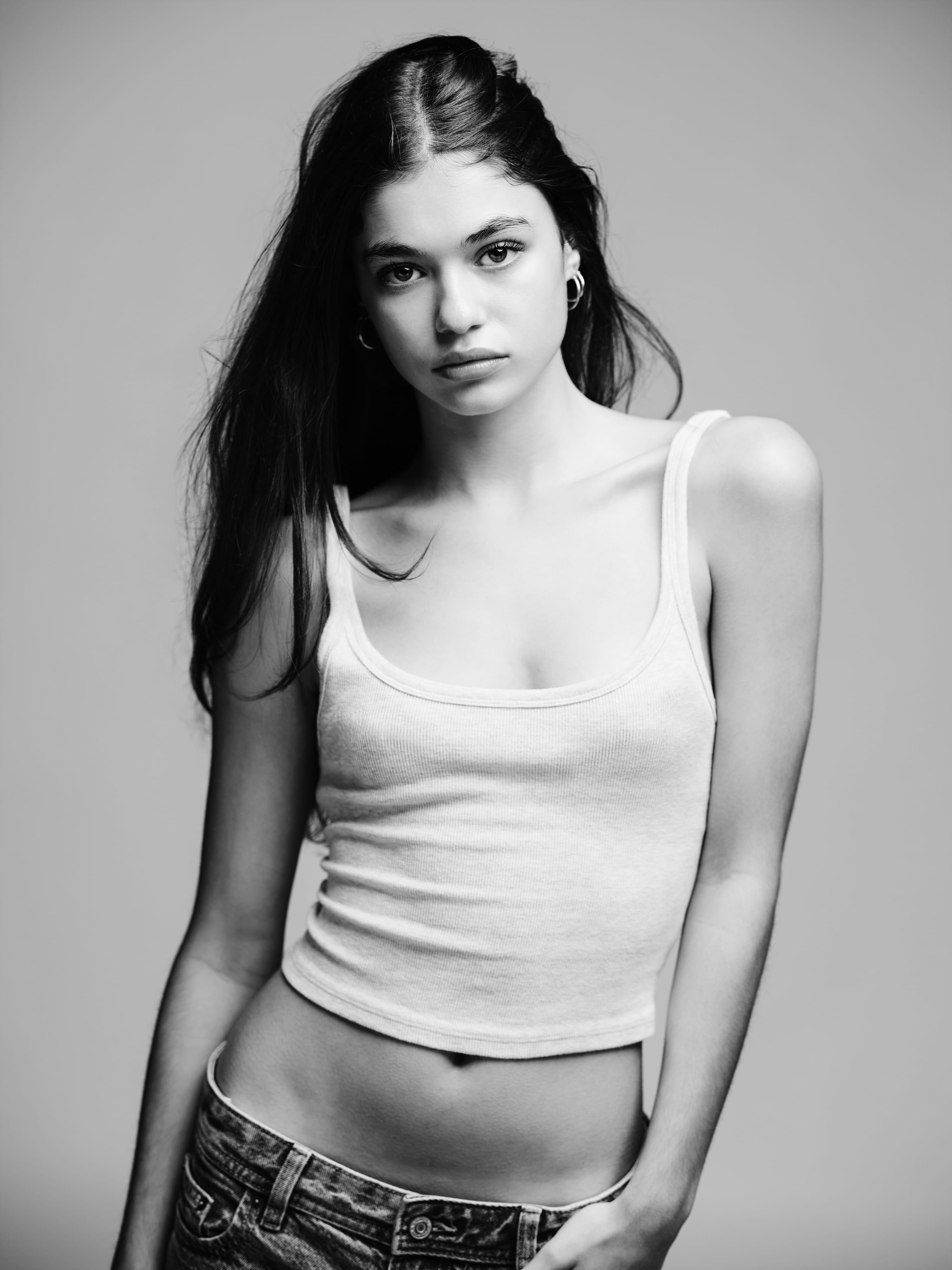 Emme Starkey in a white tank top and hoop earrings, hair half pulled back, looking into the camera, black and white