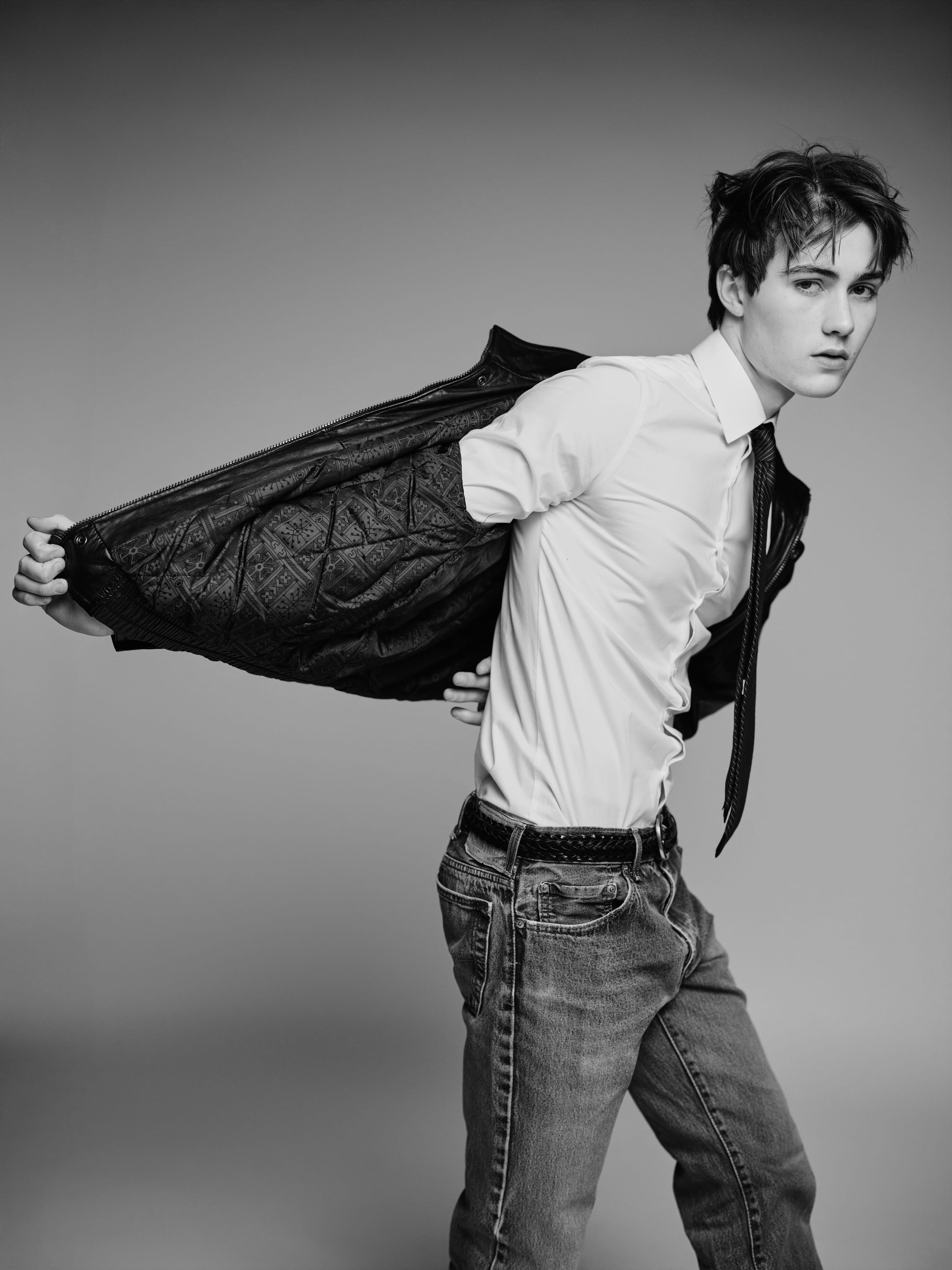Greyson pulling a leather jacket off behind him, white shirt and tie, black and white