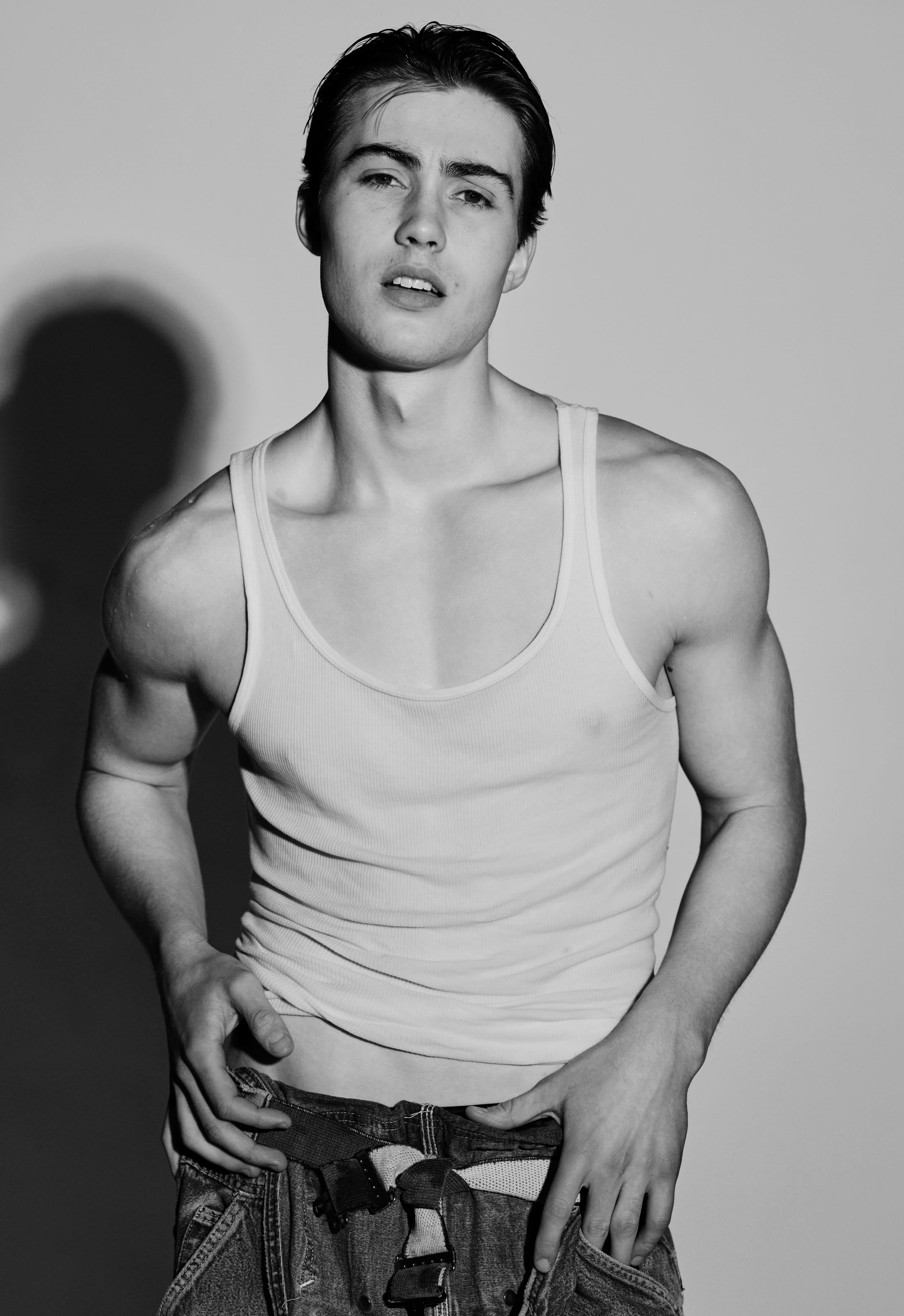 Greyson in a white tank facing the camera, hard shadow behind him, black and white