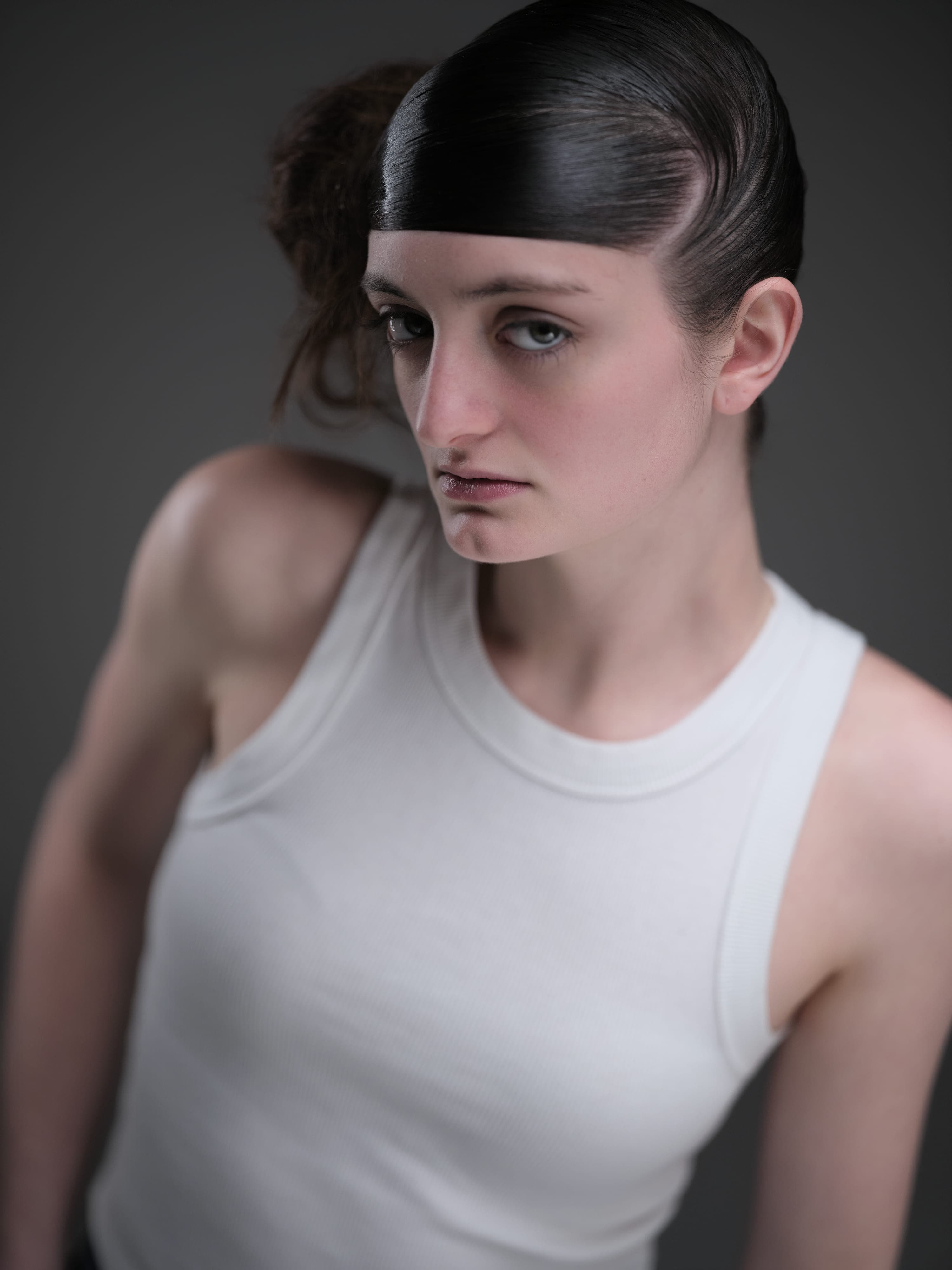 Maddie with hair slicked and knotted, hand at her shoulder, studio