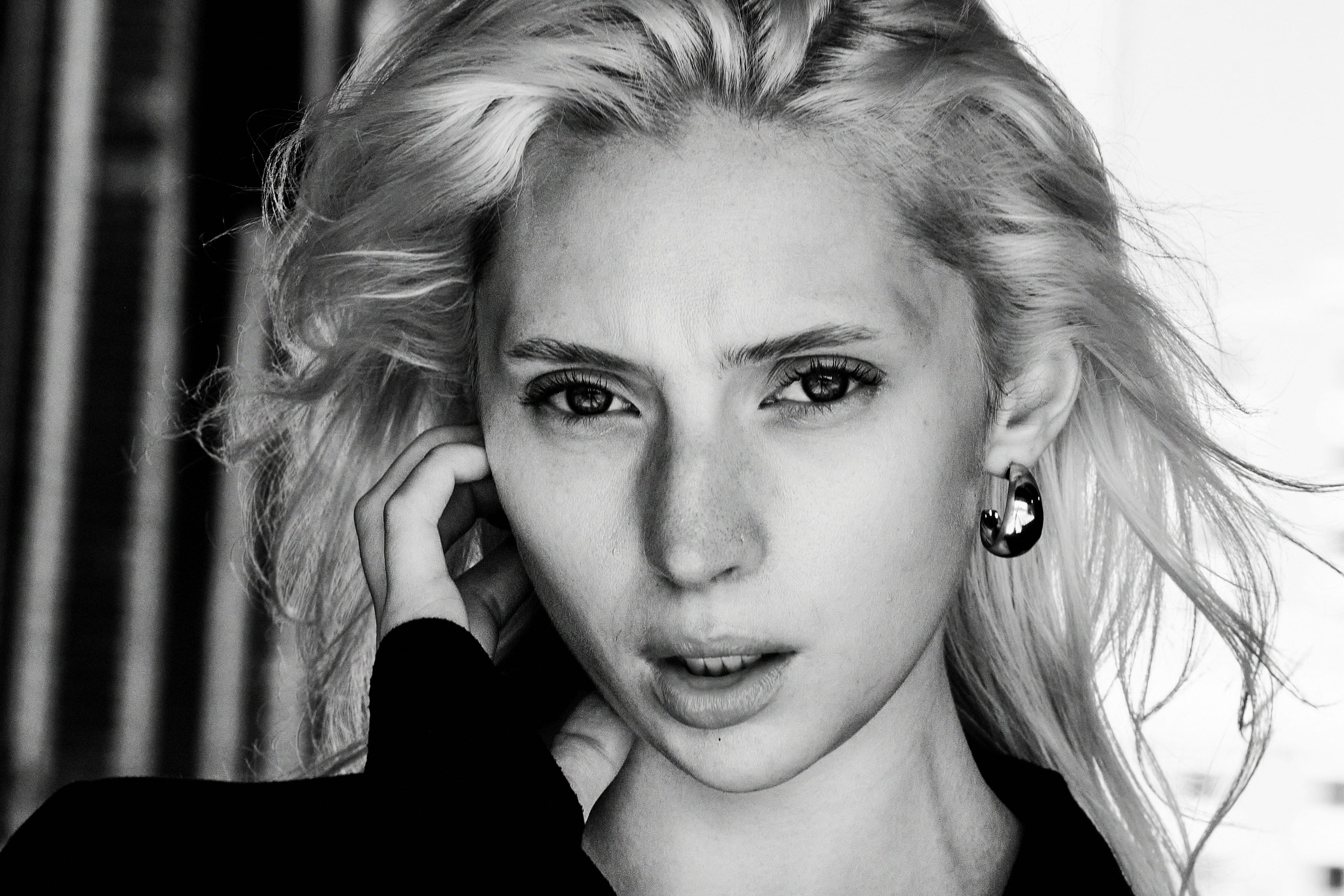 Nat Zahari looking straight into the camera, windswept platinum hair, hand at her ear, black and white, from ONE WAY